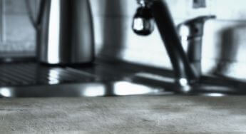 Blurred kitchen sink area with a faucet, a metal kettle, and a clean countertop.