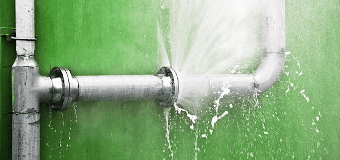 A metal pipeline against a green wall, spraying water from a joint due to a visible leak, highlighting the need for plumbing repair or maintenance.