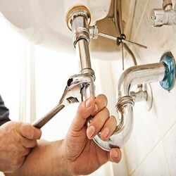Technician plumber using a wrench to repair a water pipe under the sink.